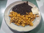 Huevos revueltos con tocino - scrambled eggs with bacon, served with fried black beans and a slice of cheese.